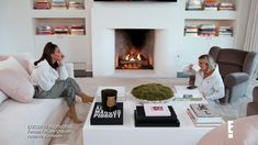 two women sitting on couches in front of a fire place