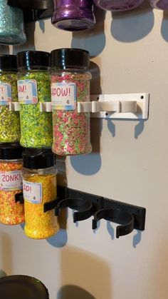 there are many different colored sprinkles in the jars on the wall next to each other