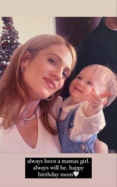 a woman holding a baby in her arms and pointing at the camera with both hands