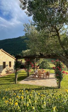 an image of a house in the middle of a field with flowers and trees around it