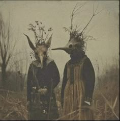 two people with masks on their heads standing in tall grass