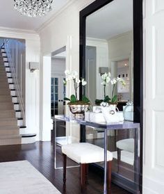 a room with a mirror, chandelier and white flowers on the table in front of it