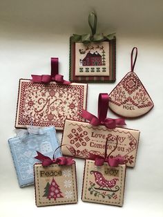 four cross stitch christmas tags with ribbons and bows hanging on the wall next to each other