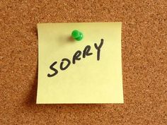 a sticky note pinned to a cork notice board with the word sorry written on it