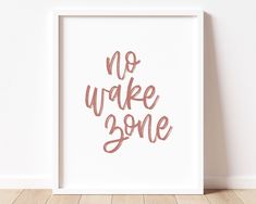 a white framed print with the words no wake some in pink ink on a wooden floor