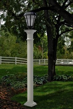 a white lamp post in the middle of a grassy area next to a tree and fence