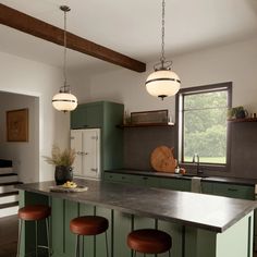 a kitchen with green cabinets and stools next to a counter top that has three lights hanging from it