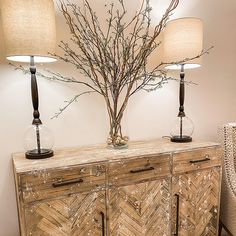 two lamps are sitting on top of a wooden cabinet next to a vase with branches in it