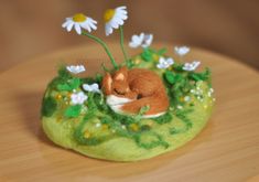 a small stuffed animal laying on top of a green patch of grass and daisies