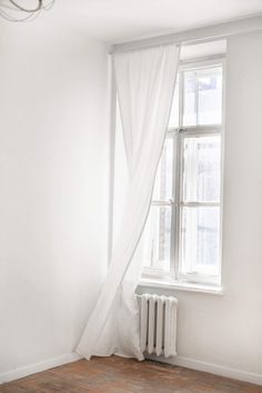 an empty room with a radiator, window and white curtains on the windowsill