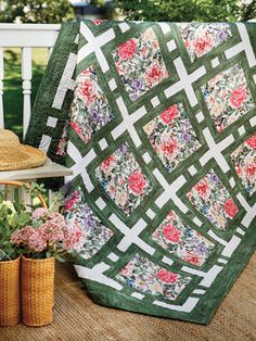 a green and white quilt sitting on top of a wooden bench next to potted plants