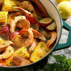 a pot filled with shrimp, potatoes and corn on the cob next to lemons