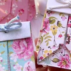 a person holding an origami box with flowers on it and a bow tied to the top