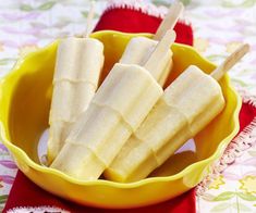 three pieces of banana are in a yellow bowl on a floral tablecloth with two wooden spoons