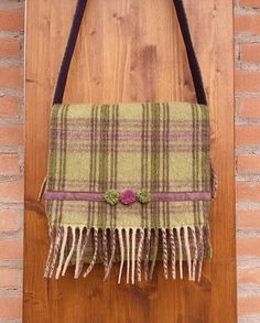 a green plaid purse hanging on a wooden door with fringes and flowers in the center