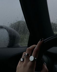 a woman is driving in the rain with her hand on the steering wheel and wearing rings