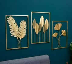 three gold metal wall art pieces on a blue wall next to a couch and plant