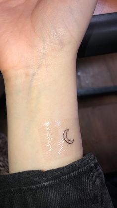 a woman's wrist with a small crescent tattoo on the left side of her arm