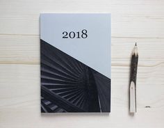 a spiral notebook next to a fountain pen on a wooden surface with the year 2018 written in black