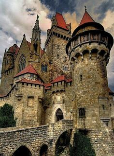 an old castle with red roof and towers on it's sides, against a cloudy sky