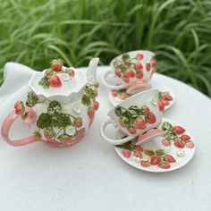 four tea cups and saucers with strawberries on them sitting on a white cloth