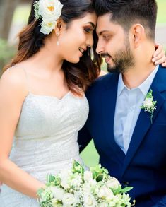 a bride and groom pose for a wedding photo in front of some trees with white flowers