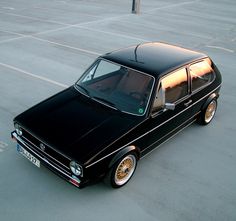 an old black station wagon is parked in a parking lot with no one around it