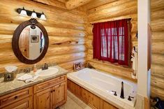 a bathroom with wooden walls and flooring has a large mirror above the bathtub