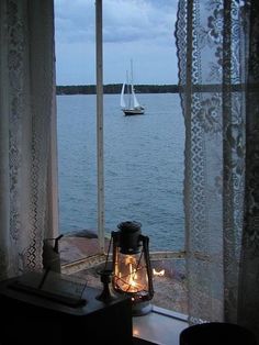 a lantern is lit on the window sill overlooking the water and sailboats in the distance