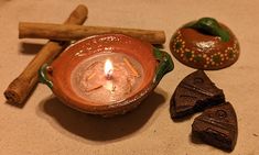 a candle is sitting in a clay bowl next to two pieces of wood and some rocks