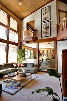 a living room filled with lots of furniture next to tall windows on top of a wooden ceiling