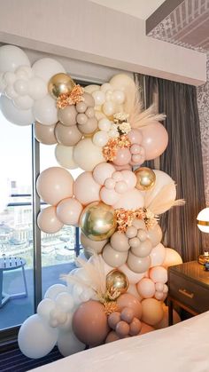 balloons are hanging from the ceiling in front of a bed and window with a cityscape behind it