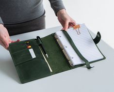 a person is holding a pen and writing on a notebook with a clipboard attached to it