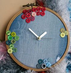 a close up of a clock made out of buttons on a blue cloth with a needle