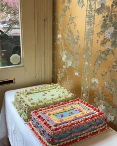 there is a large cake on the table in front of the window and wall paper behind it