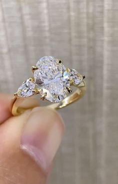 a person holding a ring with three pear shaped diamonds on it's sides, in front of a white background