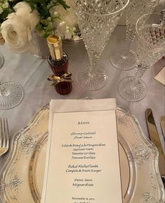 a table setting with wine glasses and silverware, menu cards and place settings on it