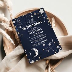 a blue and white wedding card with the words in the stars written on it next to some feathers