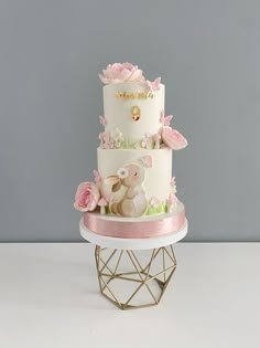 a three tiered cake with pink flowers and a teddy bear on the top layer