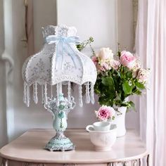 a table with flowers and a lamp on it next to a vase filled with pink roses