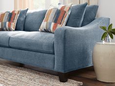 a blue couch sitting on top of a wooden floor next to a white potted plant