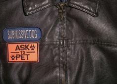 a black leather jacket with a patch on the back saying submissive dog ask to pet