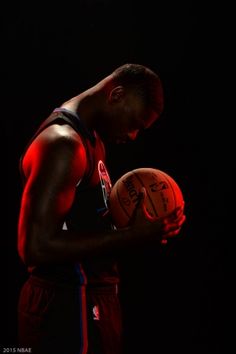 a man holding a basketball in his right hand while standing against a black background with red lighting