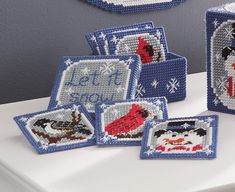 cross stitched coasters with pictures of birds and snowflakes on them, sitting on a white surface