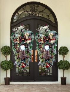 two christmas wreaths on the front door of a house with potted plants and trees