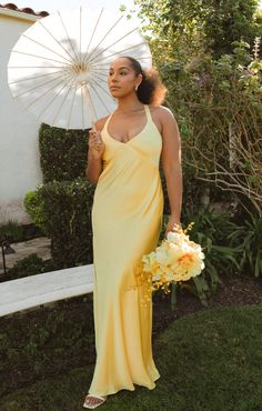 a woman in a long yellow dress holding an open white parasol and flower bouquet