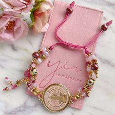 a pink bracelet with a gold medallion and beads on it sitting next to some flowers