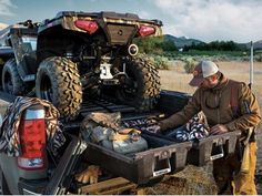 two men loading items into the back of a four - wheeler truck in a field