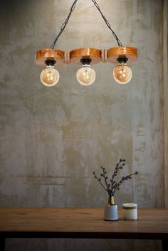 a wooden light fixture hanging from the ceiling above a table with two vases on it