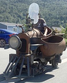 a man riding on the back of an old fashioned steam powered vehicle in front of a blue car